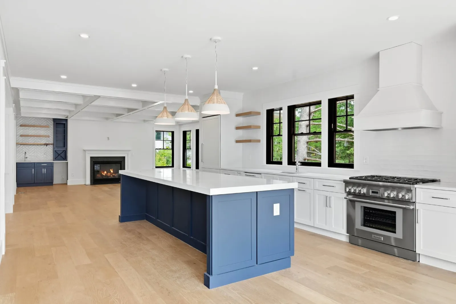 Kitchen with a blue island, white shaker cabinets, pro-style range, white hood, open to a fireplace room