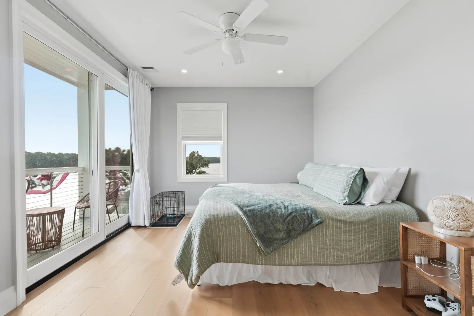 Bedroom with sliding glass doors to a balcony overlooking the water, a ceiling fan, light hardwood floors and a queen bed